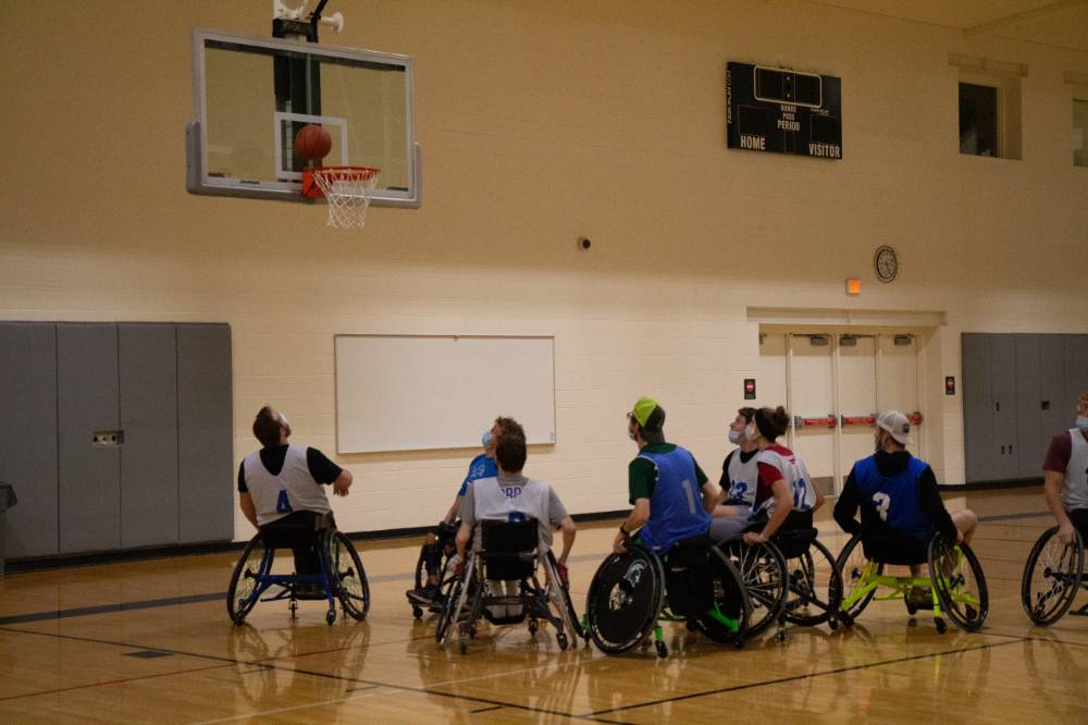 Group of adults in wheelchairs underneath basketball hoop with the ball near the rim.